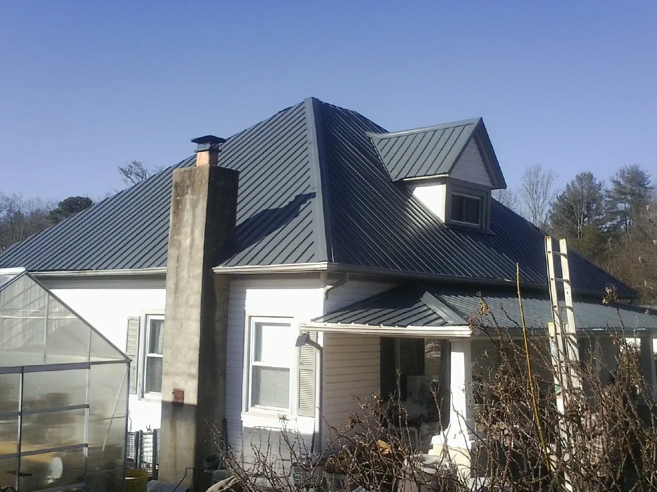 Dark blue standing seam metal roof on a white farmhouse with dormer — Slate & Tile Roof Repair by Roofing Brothers in Sioux Center