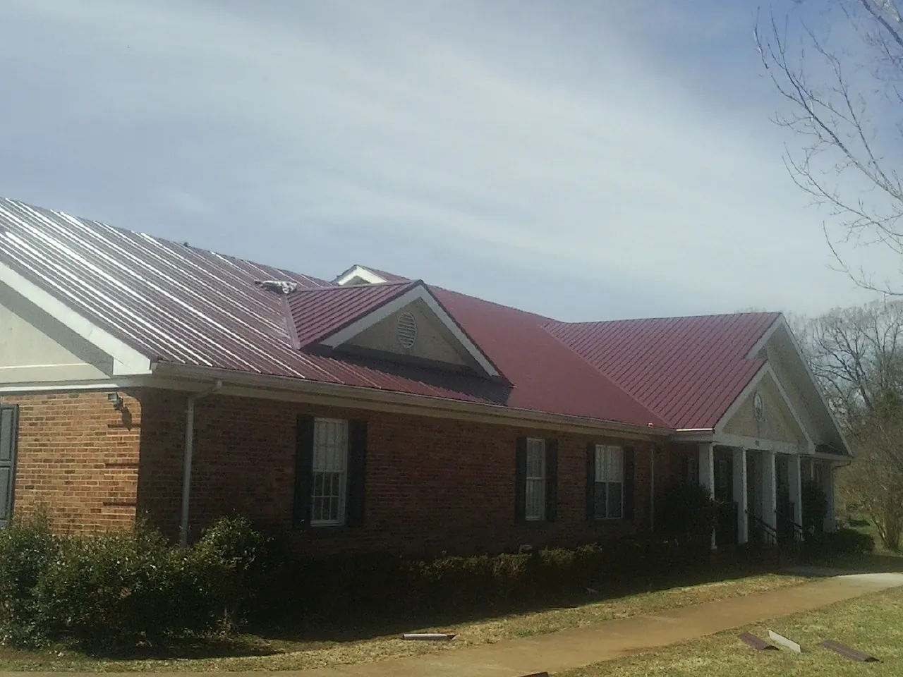 Red metal roof with gabled entries on a long brick building, from a Hail Damage Roof Repair job in Sioux Center