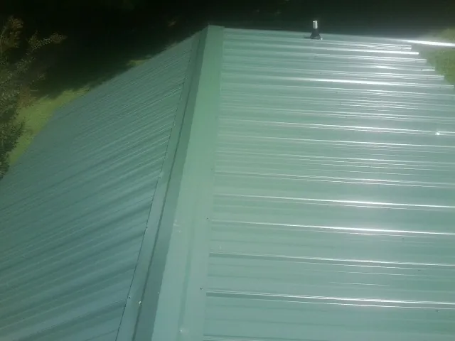 New green metal panels meeting at the ridge of a roof — Flat Roof Repair work by our crew in Sioux Center