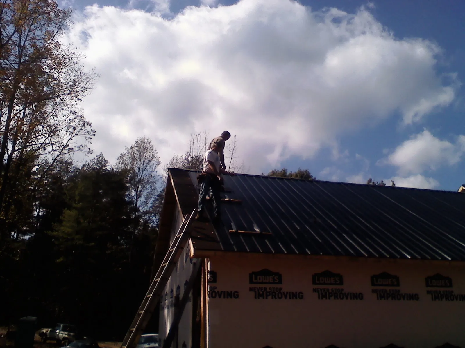 Roofer fastening dark metal panels high against a cloudy sky, from a Roof Inspection job in Sioux Center