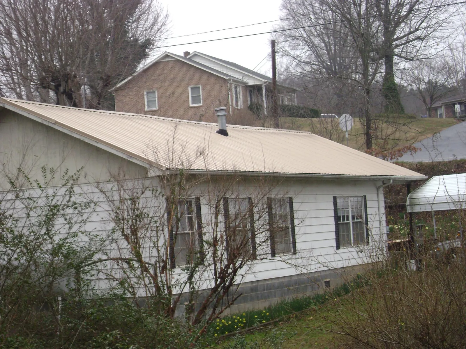 Tan metal roof on a white sided house set into a hillside — Commercial Roofing by Roofing Brothers in Sioux Center